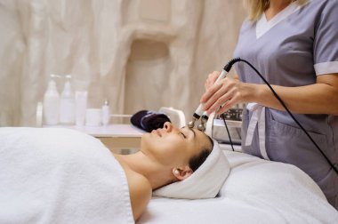 Kadının yüz masajı spa prosedürünün yan görüntüsü. Elektrikli yüz bakımı. Mikroakım kaldırma suratı. Güzellik spa prosedürü. Sağlık odasında yaşlanma karşıtı gençleştirme cerrahi olmayan tedavi