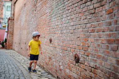 Eski tuğla duvarın yanında 6 yaşında sarışın bir çocuk.