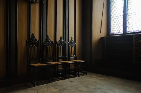 four chairs in a dark room of a castle near the window