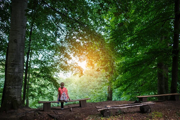 a girl sitting on a bench in the forest