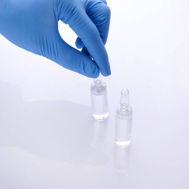 Mavi eldivenli bir doktorun eli beyaz arka planda iki ampulden birinin üst kısmını tutuyor.