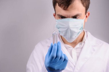 Beyaz üniformalı bir doktor elinde mavi eldivenle tuttuğu ampulü ilaçla inceliyor.