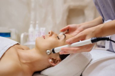 Kadının yüz masajı spa prosedürünün yan görüntüsü. Elektrikli yüz bakımı. Mikroakım kaldırma suratı. Güzellik spa prosedürü. Sağlık odasında yaşlanma karşıtı gençleştirme cerrahi olmayan tedavi