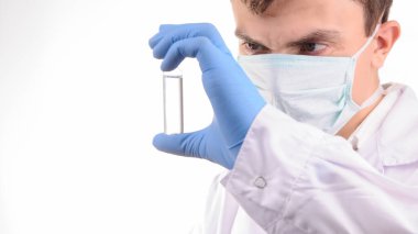 Beyaz üniformalı bir doktor elinde mavi eldivenle tuttuğu ampulü ilaçla inceliyor.