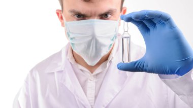 Beyaz üniformalı bir doktor elinde mavi eldivenle tuttuğu ampulü ilaçla inceliyor.