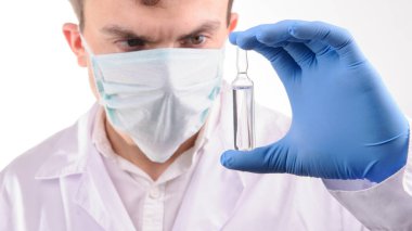 Beyaz üniformalı bir doktor elinde mavi eldivenle tuttuğu ampulü ilaçla inceliyor.