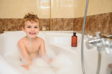 Küçük çocuk banyo küvetinde köpük ve sabun köpüğüyle yıkanıp oynuyor.