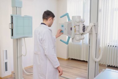  Bir erkek radyologun muayene odasındaki röntgen cihazını ayarlarken ki arka görüntüsü.