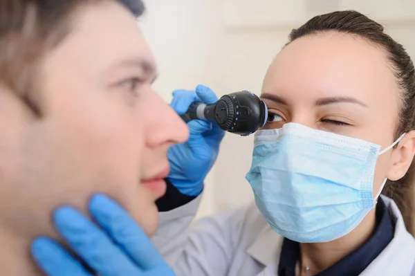 close up photo of a optometrist examining man\'s eyes with ophthalmoscope