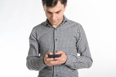 Beyaz arka planda gri kıyafetli 30 yıllık esmer bir adam cep telefonuna mesaj yazıyor.