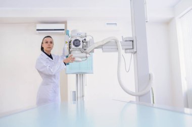 Bir kadın radyologun ön görüntüsü muayene odasında röntgen cihazını ayarlıyor.