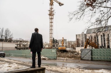 Klasik montlu genç bir adamın inşaat alanına bakışının arkası.