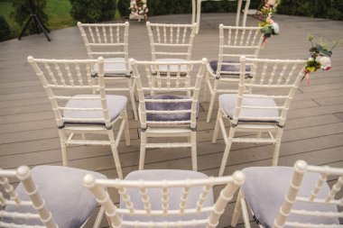 Bahçedeki bir düğün töreninde çiçeklerle süslenmiş beyaz sandalyelerin üst görüntüsü.