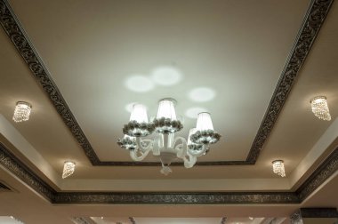 Beyaz ve altın renginde klasik bir tavanın fotoğrafını çek ve üzerine bir avize as asılmış.