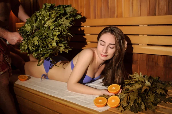 나무로 사우나에 오렌지와 자작나무 빗자루로 맛있게 마사지를 아름다운 여인의 — 스톡 사진