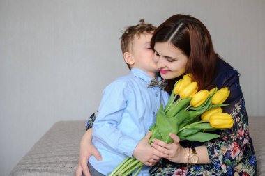 Elinde sarı laleler olan bir çocuğun mutlu annesine sarıldığı fotoğrafı.