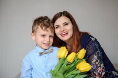 Elinde sarı laleler olan bir çocuğun mutlu annesine sarıldığı fotoğrafı.