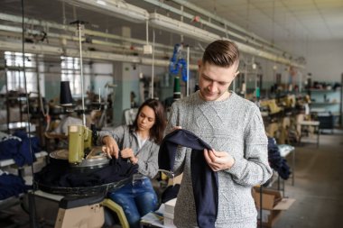 Bir iş parçasını analiz eden genç bir adamın ve tekstil endüstrisinde örgü ören makineyle çalışan bir kadının fotoğrafını çek.
