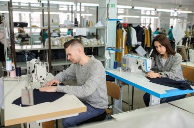 Bir fabrikada dikiş makinesiyle dikiş diken genç bir adam ve diğer terzilerin fotoğrafını çek.