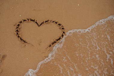 Sahilin kumlarına çizilmiş bir kalp dalgası ve güneş ışığı