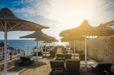 Yaz tatili için cennet gibi bir tropik tatil beldesindeki kumsalda Thatched plaj şemsiyeleri ve şezlongları