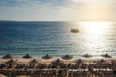 Yaz tatili için cennet gibi bir tropik tatil beldesindeki kumsalda Thatched plaj şemsiyeleri ve şezlongları