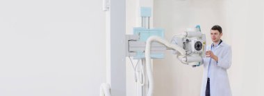 Genç doktor radyoloji uzmanı röntgen cihazını ayarlayıp röntgen radyografisi için hazırlıyor. Metin için boşluk kopyala