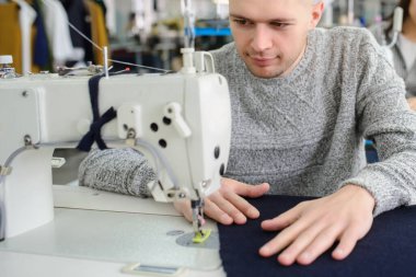 Bir fabrikada dikiş makinesiyle dikiş diken genç bir adamın fotoğrafını çek.