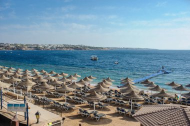 Yaz tatili için cennet gibi bir tropik tatil beldesindeki kumsalda Thatched plaj şemsiyeleri ve şezlongları