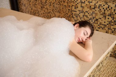 Beyaz köpüklü genç bir kadının hamamda rahatladığının en üst görüntüsü.