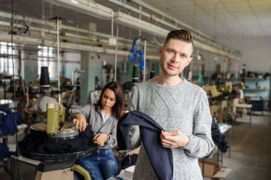 Bir iş parçasını analiz eden genç bir adamın ve tekstil endüstrisinde örgü ören makineyle çalışan bir kadının fotoğrafını çek.