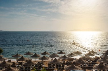 Yaz tatili için cennet gibi bir tropik tatil beldesindeki kumsalda Thatched plaj şemsiyeleri ve şezlongları