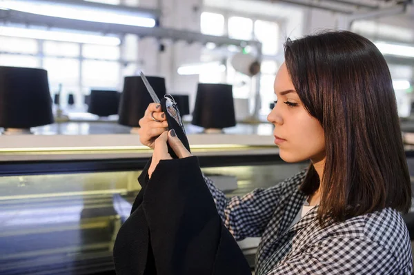 lateral view of a young woman analyzing a knitted piece of cloths near industrial knitting machine with black cones on it