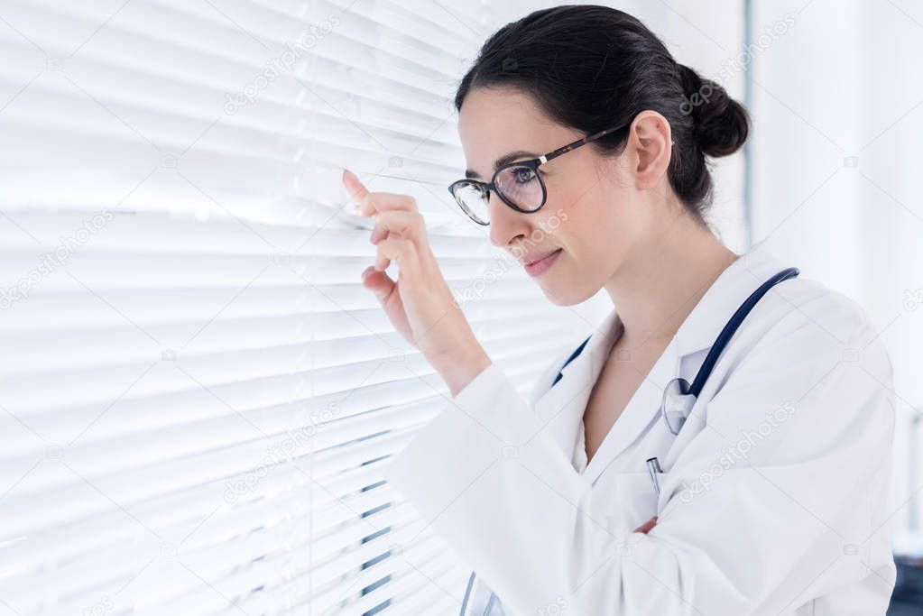 Young female physician smiling while looking through the window 