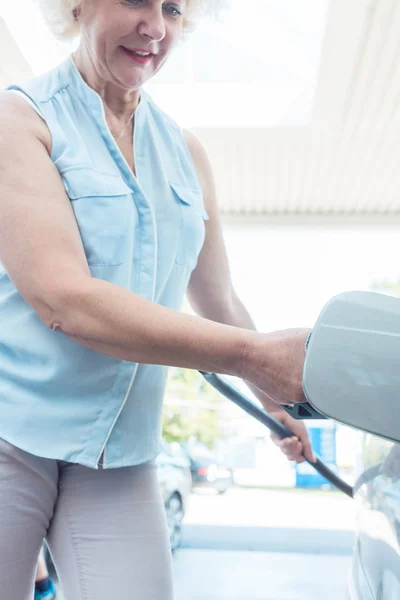 Активная пожилая женщина улыбается, заправляя бензобак своей машины — стоковое фото