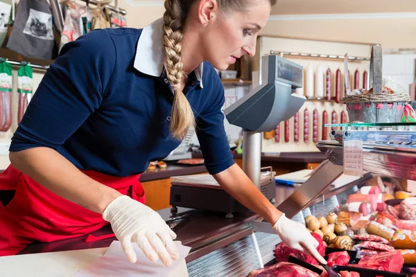 Mujer de ventas en carnicería poniendo diferentes tipos de carne en exhibición —  Fotos de Stock