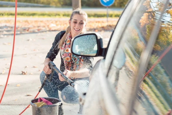 Donna che usa l'ugello ad alta pressione per pulire la sua auto — Foto Stock