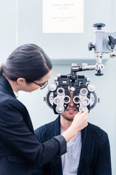 Optik a muž na oční vyšetření s phoropter — Stock fotografie