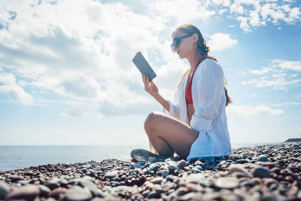 Donna che legge un romanzo su ebook vicino al mare — Foto Stock