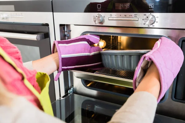 Woman putting cake into oven of kitchen — Stock Photo, Image