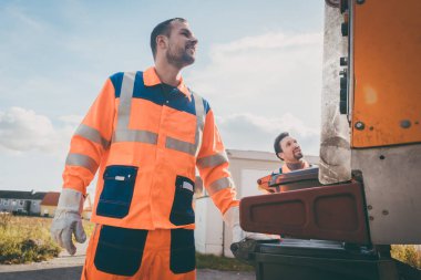 Two refuse collection workers loading garbage into waste truck clipart