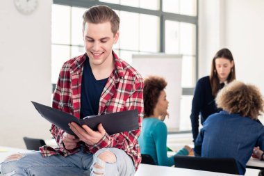 Kolej veya üniversite, sınıfta tatilinde bir masada otururken bir klasör aç holding neşeli bir yakışıklı öğrenci portresi