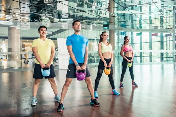 Vista completa de cuatro personas alegres sosteniendo pesas durante el entrenamiento — Foto de Stock