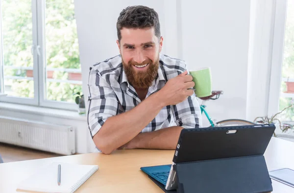 Porträtt av en säker egenföretagare ung man sitter vid skrivbord — Stockfoto