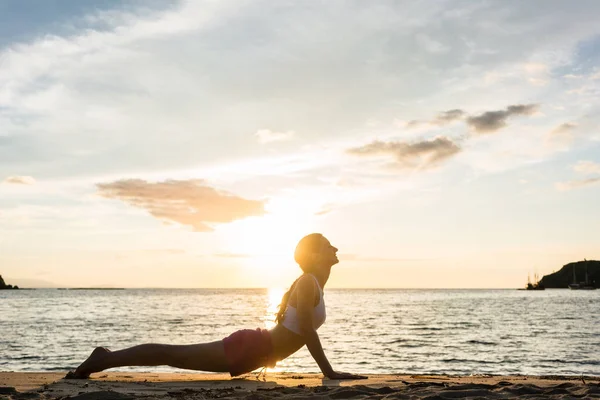 Mujer en forma practicando estiramiento a través de la pose de cobra yoga en una playa tropical —  Fotos de Stock