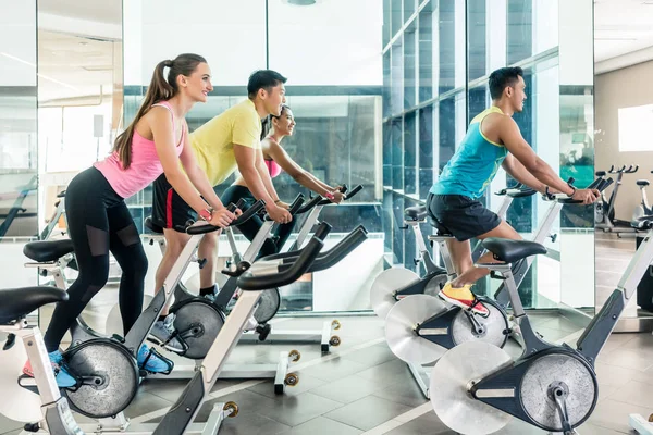 Ajuste as mulheres queimando calorias durante a aula de ciclismo em casa no clube de fitness — Fotografia de Stock