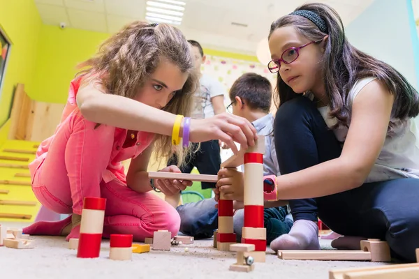 Zwei Mädchen spielen im Kindergarten mit Holzspielzeugklötzen auf dem Boden — Stockfoto