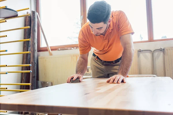 Carpenter polishing and varnishing a table — Stock Photo, Image