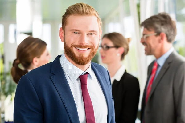 Empresário sorridente e sua equipe em segundo plano — Fotografia de Stock