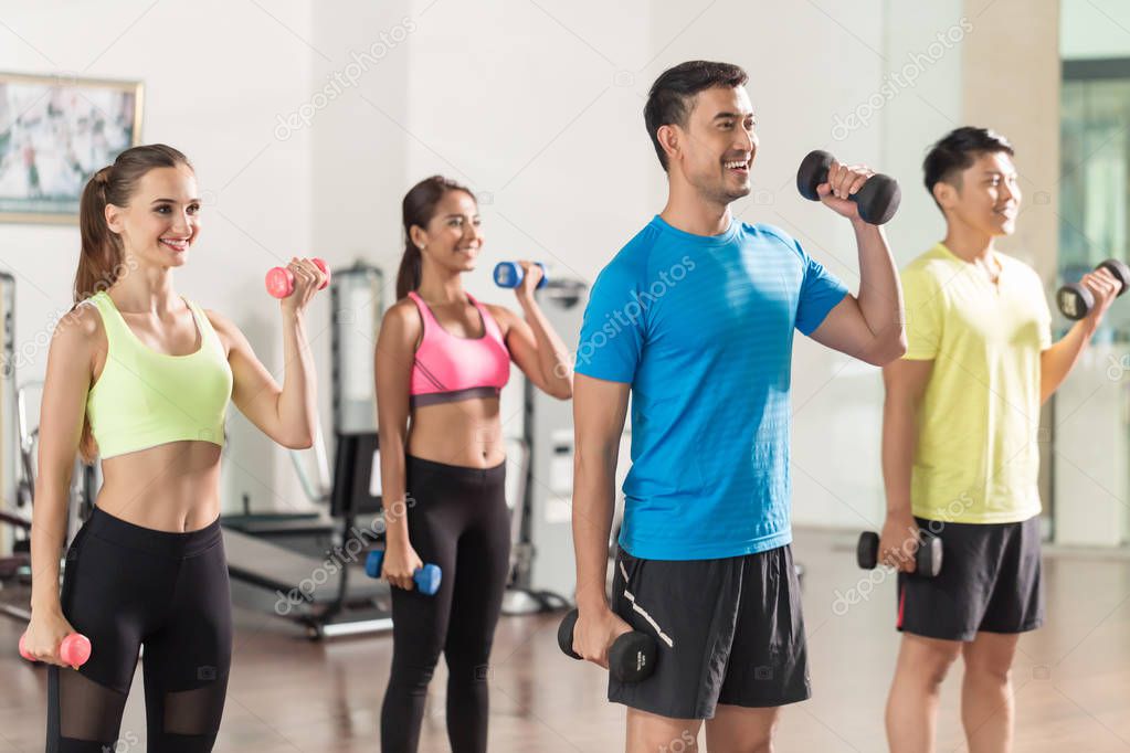 Fit handsome man smiling while exercising bicep curls during group workout